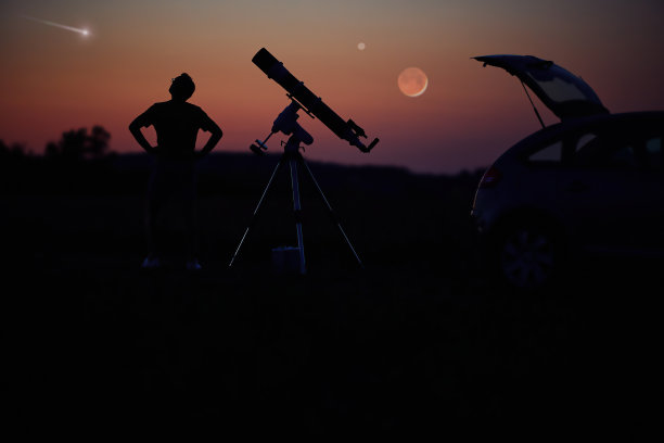 一个人的剪影，汽车，望远镜和乡村在星空下。图片下载