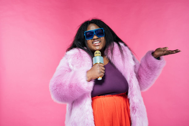 一个美丽的女人穿着毛茸茸的外套，在粉红色的背景下摆姿势图片下载