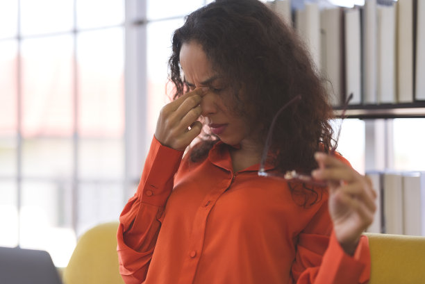 穿着橙色衬衫的黑人女性在家里的沙发上有压力和头痛的办公室综合症，在家里工作的商业女性和自由职业者传播冠状病毒covid-19图片下载