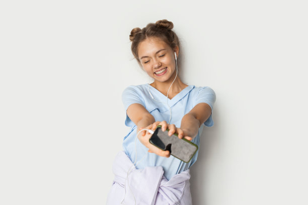 微笑的女人在白色背景下用智能手机听音乐的肖像。双手伸向相机拿着手机。闭上眼睛。享受生活。图片下载