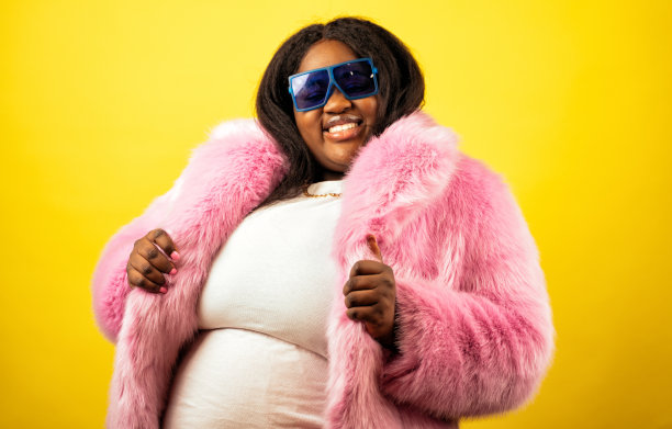 一个穿着毛皮大衣的美丽女人在黄色背景上摆姿势的照片图片下载