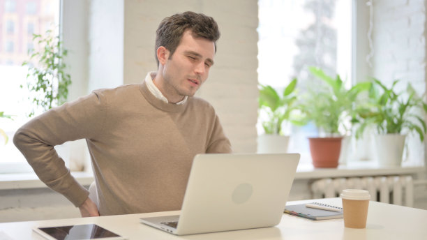 一名男子在办公室使用笔记本电脑时背痛图片下载