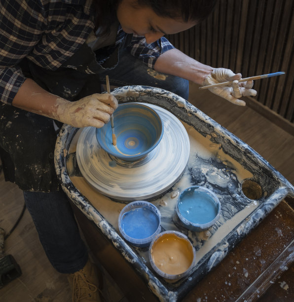 一个年轻女人的手用陶轮做陶器，给碗上色，上釉。图片下载
