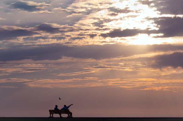 两个人坐在街边的长椅上，看那戏剧性的日落图片下载