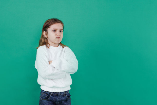 一个长头发的男孩带着委屈的表情站在绿色孤立的背景上。幼稚的悲伤图片下载
