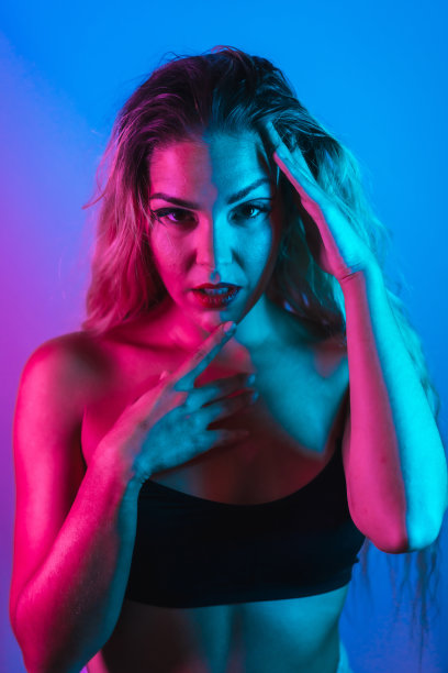 一个金发白种人女孩在夜店里画着眼睛，睫毛被安排在蓝色的背景和粉红色的霓虹灯下，看着镜头图片下载