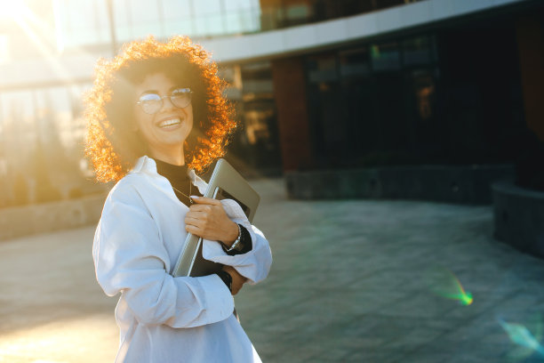 戴着眼镜，拿着平板电脑和笔记本电脑在外面摆姿势的白人商人。日落。卷发图片下载