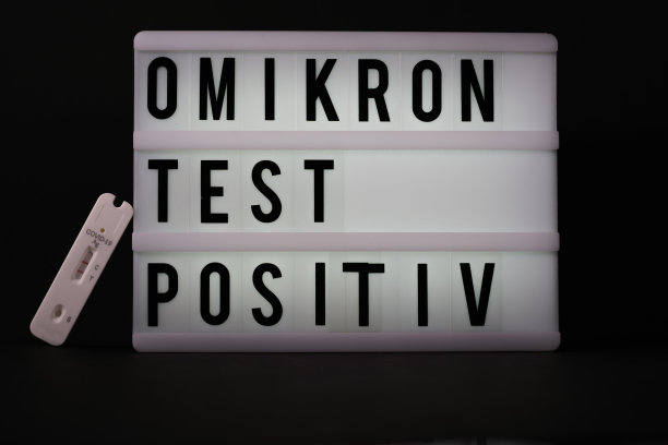 在一块刻有“Omikron检测阳性”字样的光板旁边，放置着一份新冠抗原快速检测阳性的纸条图片下载