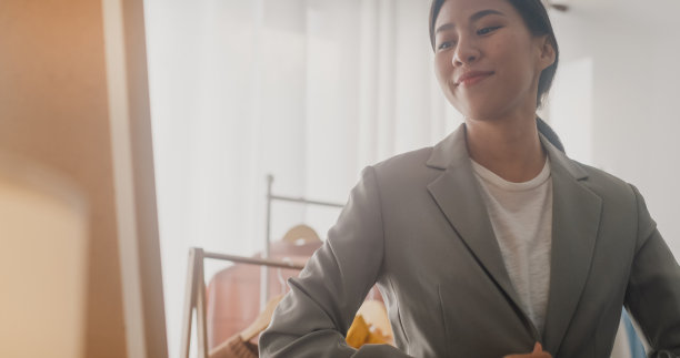 美丽年轻的亚洲妇女选择衣服在衣架上穿衣打扮自己在客厅在家里的镜子。近距离射杀。图片下载