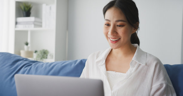 年轻的亚洲女性在家里客厅的沙发上用笔记本电脑与客户进行视频通话。图片下载