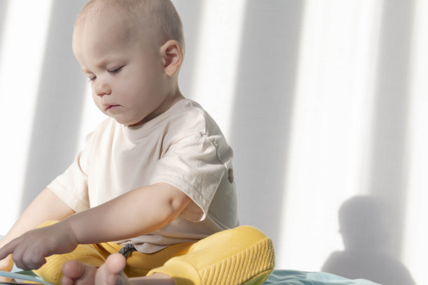 一个小男孩坐在床上的蓝色毯子上玩一部现代手机。图片下载