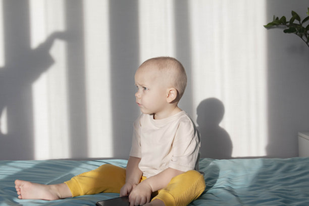 一个小男孩坐在床上的蓝色毯子上玩一部现代手机。图片下载