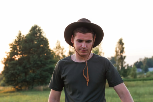 年轻的农民戴着牛仔帽在夕阳下的农田。千禧一代戴着帽子的男人的特写肖像，站在自然背景下，户外。牛仔,狂野的西部图片下载