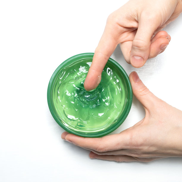 芦荟凝胶在一个女性的手，这是从一个罐子里舀出来的白色背景，顶部的视图。芦荟是治疗晒伤的天然药物。自然的替代医学。图片下载