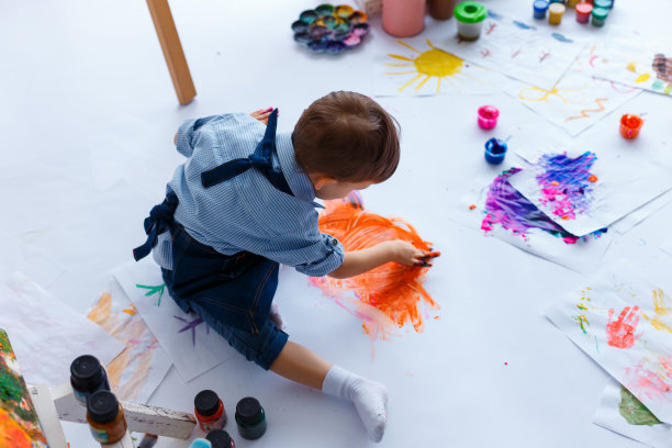 可爱、快乐、穿着蓝色衬衫和牛仔裤的白人男孩，用明亮的手指颜料在纸上画画。小孩在艺术家工作室画画。幼儿教育理念，幸福家庭，创造图片下载