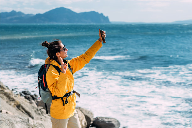 一个旅行者拿着手机站在大海的背景上。一个小女孩以大海、山脉和天空为背景摆出姿势。旅行和发现地球偏远的角落。本空间图片下载
