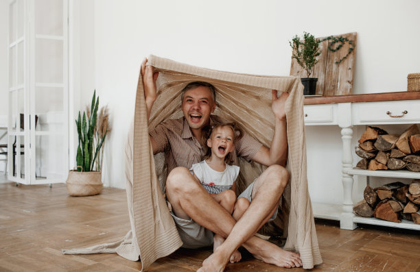 一位快乐的父亲和他的小女儿在地板上用毯子搭帐篷玩耍。图片下载