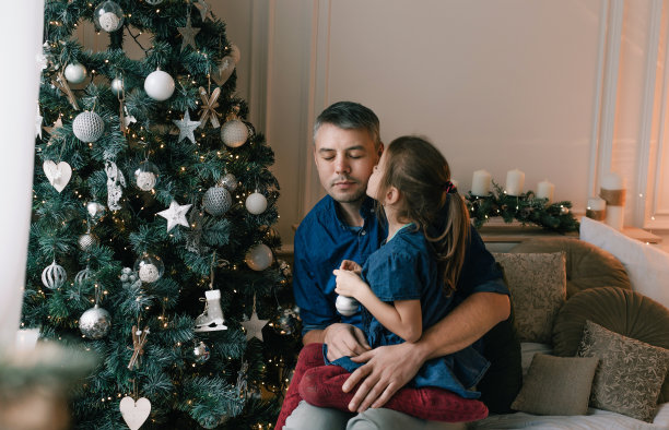 在装饰圣诞树的时候，小女儿轻轻地亲吻了爸爸的脸颊。等待魔法图片下载