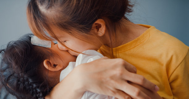 幸福快乐的亚洲家庭妈妈抱着生病的蹒跚学步的女孩，在客厅里贴上退热凝胶，亲吻婴儿的额头。医疗保险、治疗和保健概念。图片下载
