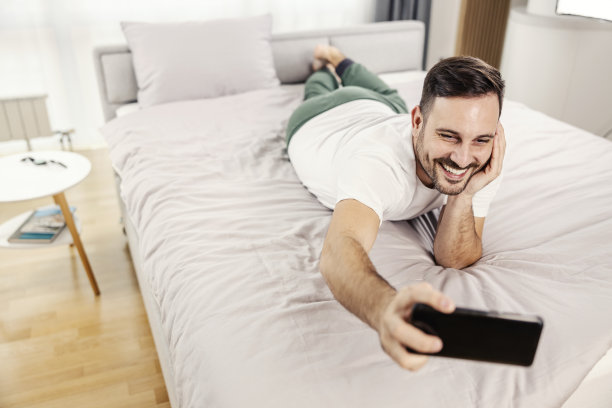 一个调情的男人躺在他舒适的家里的床上自拍。图片下载