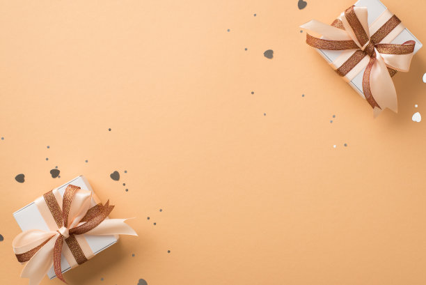 俯视图照片的情人节装饰白色礼品盒与发光的棕色和浅米色丝带蝴蝶结银色心形纸屑和亮片在孤立的米色背景与空白空间图片下载
