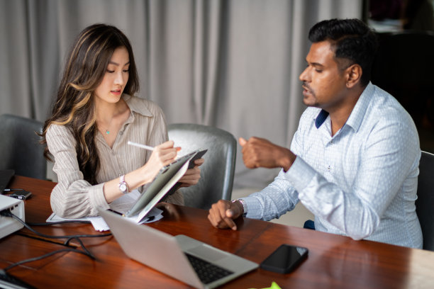 会议照片中，一名亚洲中国女性与印度男同事讨论平板电脑图片下载