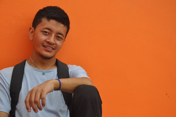 一个快乐的亚洲人看着相机，坐在橙色的墙壁背景与复制空间图片下载