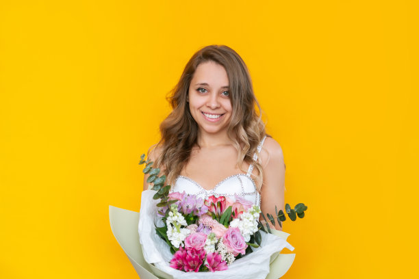 一个年轻的金发碧眼的女人，一头卷发，面带微笑，手里拿着一束花，花束装在一个时尚的包里图片下载