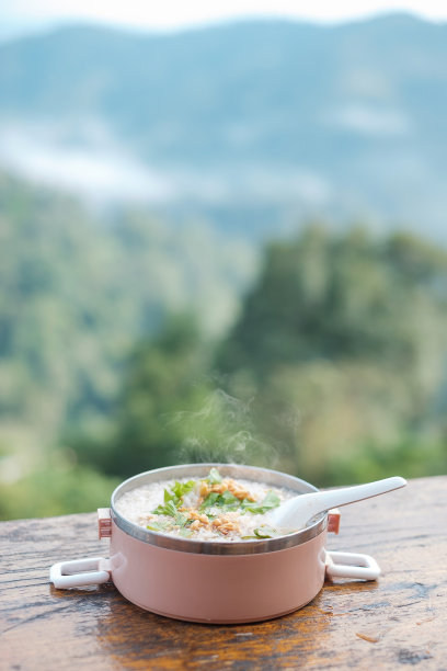 在山景城的背景下，木桌上放猪肉粥或米饭汤，配上猪肉和蔬菜图片下载