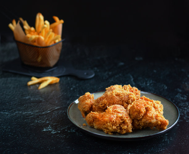 在陶瓷盘子上撒上面包屑的辣炸鸡翅。背景里有薯条。黑色背景的照片。低调。极简主义。有选择性的重点。图片下载
