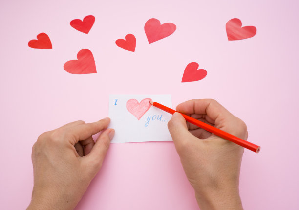 女孩的手正在准备情人节的礼物，用红铅笔在粉红色的背景上画了一张情人节卡片图片下载