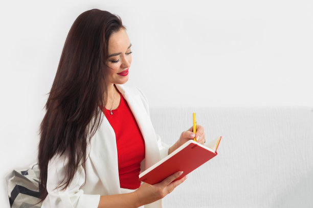 优雅微笑的女人坐在沙发上写在记事本上图片下载