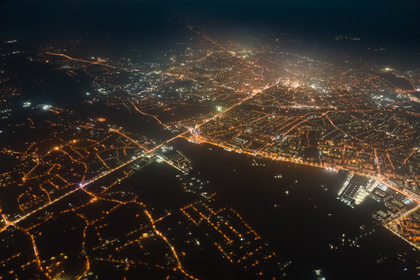 夜间从飞机窗口鸟瞰城市住宅区的建筑物和灯火通明的街道。高海拔地区黑暗的城市景观图片下载