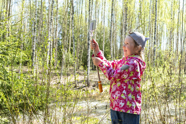 一个白人小孩在春天的森林里散步。一个5岁的小女孩用手机拍照片和视频。图片下载