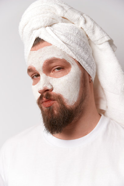 身穿白色t恤的男子敷面膜，以白色为背景站立。美容、美容、健康理念图片下载