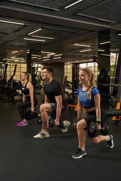 三个健壮的年轻人在体育馆里举着哑铃蹲着图片下载