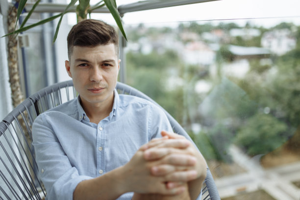 一个年轻人坐在阳台的椅子上图片下载