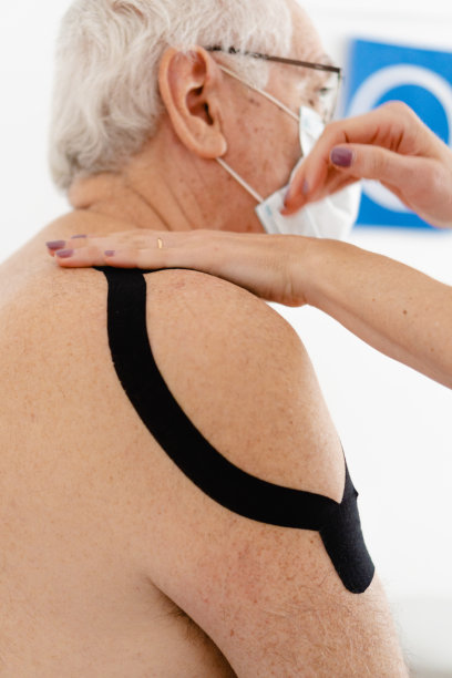 职业治疗师，运动机能学家，用轻拍法治疗一个老人肩膀上的肌腱炎，垂直的照片图片下载