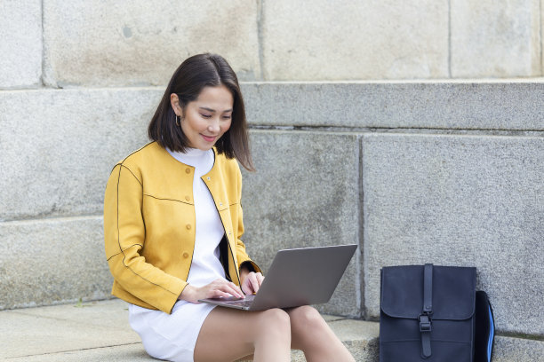 美丽的亚洲妇女使用笔记本电脑。微笑的亚洲女孩坐在楼梯上使用笔记本电脑。使用手提电脑的亚洲女商人图片下载