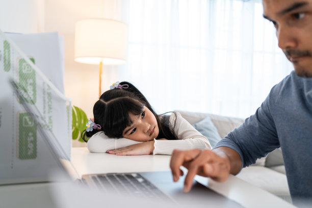 亚洲小女孩感到悲伤，需要和忙碌的父亲玩。有魅力的爸爸在新常态下使用笔记本电脑在家工作，没有时间照顾小女孩。图片下载