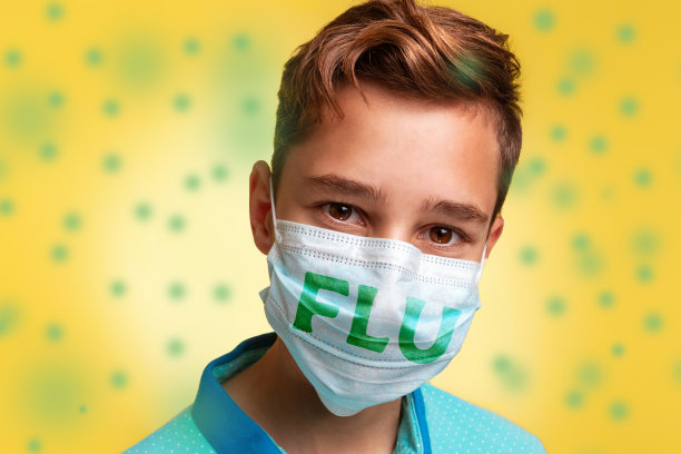 预防病毒和疾病的概念。这是一个十几岁的男孩的特写照片，他穿着一件蓝色的t恤，戴着印有“流感”字样的口罩。黄色背景与绿色细菌图片下载