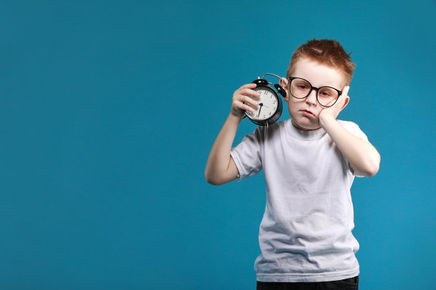 小男孩醒来，闹钟，孤立在蓝色背景。定义你自己的生活节奏。快乐的时间概念。计划和时间图片下载