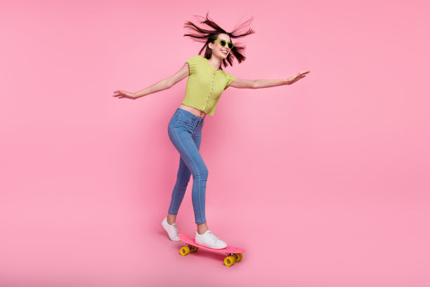 全尺寸照片无忧无虑微笑的女孩骑滑板与飞扬的头发极端孤立在粉红色的背景图片下载