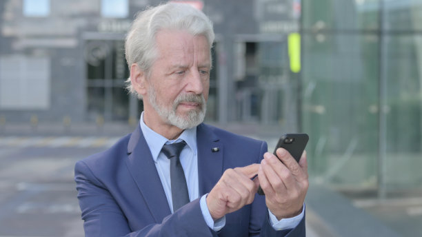 老商人站在户外使用智能手机图片下载