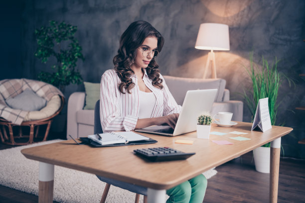 甜美迷人的年轻女士的照片，戴白色衬衫眼镜打字现代小工具，坐在桌子室内室内房间的家图片下载