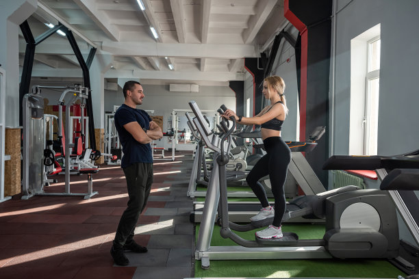 一个漂亮的年轻女子来到健身房，在一位合格的教练的指导下做腹部按压。图片下载