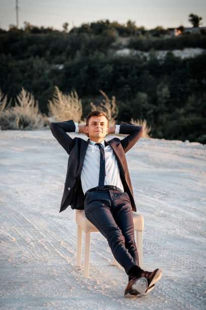 一个年轻人穿着一件经典的夹克，双手放在脑后，坐在椅子上休息。图片下载