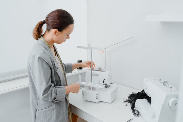 年轻的女裁缝用厘米的缎带在脖子上正在调整桌子上的套衫机/哔子布图片下载