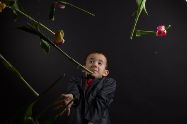 一个患有白癜风的男孩，穿着红色的t恤，灰色的夹克，拿着一束黄色的郁金香图片下载