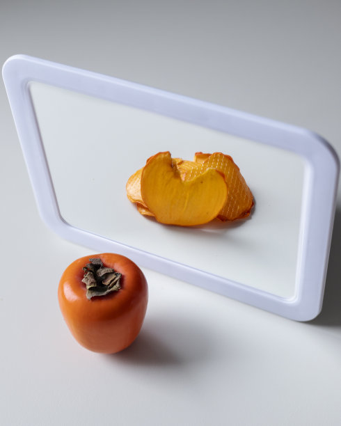 橙色的柿子在白色的背景和干燥的柿子的反射在一个白色的镜子图片下载